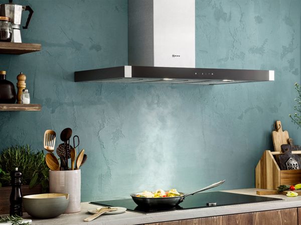 Cucina con piano cottura a induzione e cappa aspirante a parete Neff, con una padella fumante 