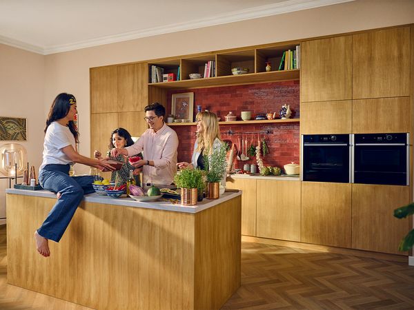 4 people are positioned around a kitchen island, actively participating in a cooking activity.