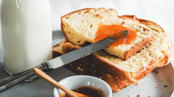 Eine Scheibe Brioche mit Orangenmarmelade, daneben ein Messer und eine Flasche Milch
