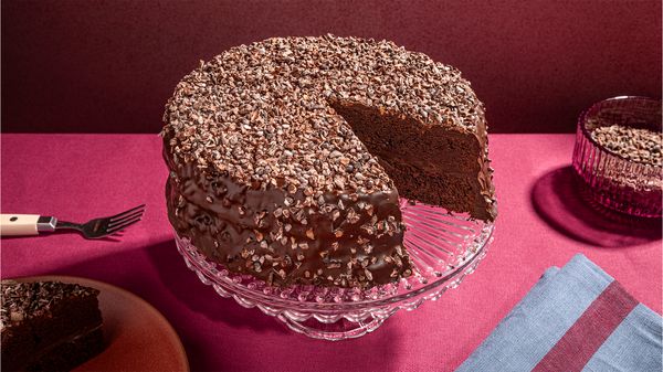 Devils food cake with a slice cut out served on a glass cake stand