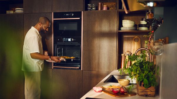 A man is preparing food in a kitchen, focused on a dish while an oven is visible in the background. 