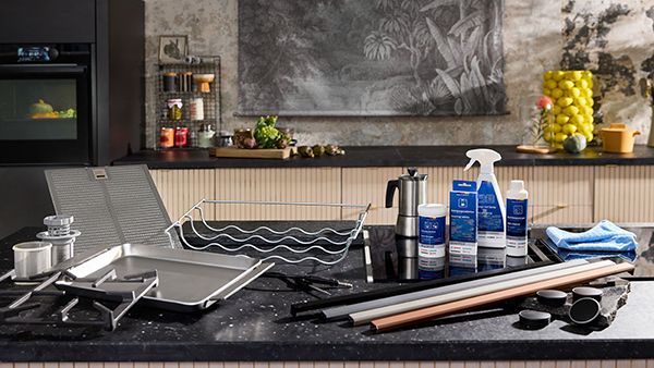 Numerous different spare parts, accessories and cleaning care items placed on dark countertop in NEFF kitchen