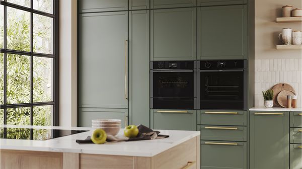 A modern kitchen featuring green cabinets, a built-in oven, and a stove for cooking. 