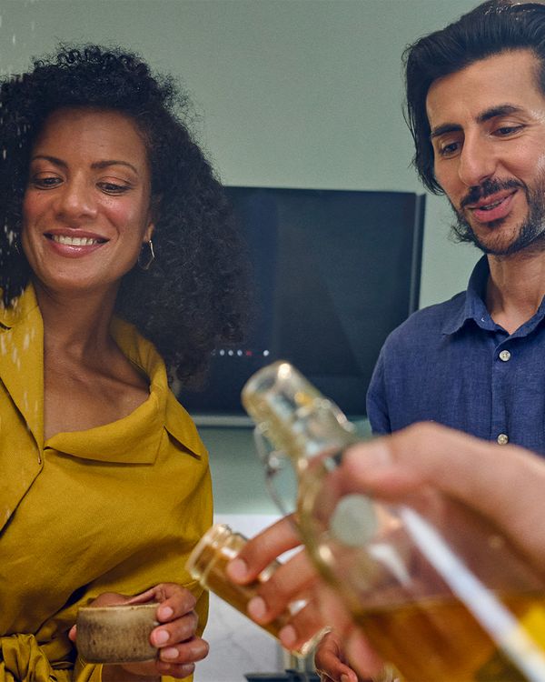 A group of people in a kitchen holding drinks and food, enjoying a social gathering while cooking together.  