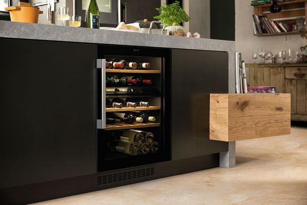 Armadio da cucina nero elegante con frigorifero per vino con ripiani in legno e cassetto, mostrando bottiglie di vino ordinate.