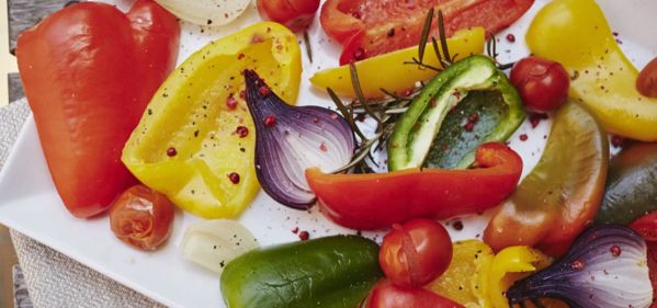 A colorful mix of bell peppers, cherry tomatoes, and onions on a white plate, garnished with rosemary and spices.