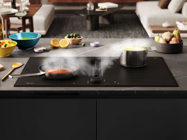 Matzwarte kookplaat met afzuiging staat aan en zuigt effectief alle stoom van de twee pannen af