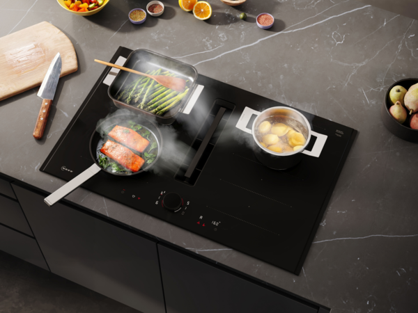 Draufsicht auf das NEFF Matt Black Induktionskochfeld mit mehreren Töpfen beim Kochen, integrierter Kochfeldabzug in Funktion.
