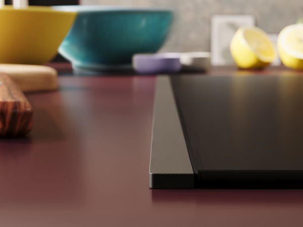 Detailansicht eines NEFF Induktionskochfelds mit Flex Design Seitenleiste in Anthracite Grey, eingebaut in eine bordeauxfarbene Arbeitsfläche.