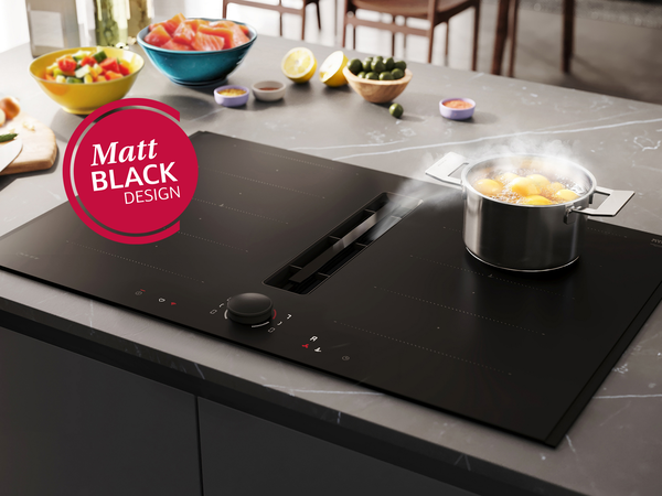 A sleek black induction hob with a pot of boiling eggs; surrounded by fresh vegetables and a knife, showcasing modern cooking design.