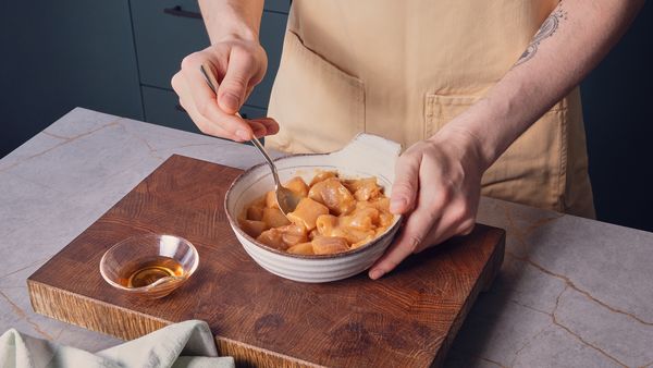 Die Hähnchenstücke werden mit der Sauce in einer Schüssel vermengt.