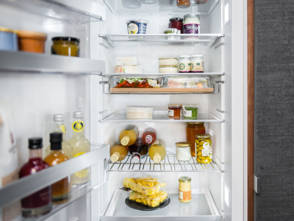 Innenraum eines NEFF Kühlschranks mit mehreren Glasablagen, GourmetTray, Flaschenlagerung auf dem Bottle Flex Shelf und einer Auswahl an frischen Lebensmitteln wie Fleisch, Obst und Getränken.
