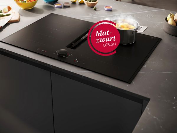 Kookplaat met afzuiging in matte afwerking met pan aardappelen op een marmeren werkblad. 