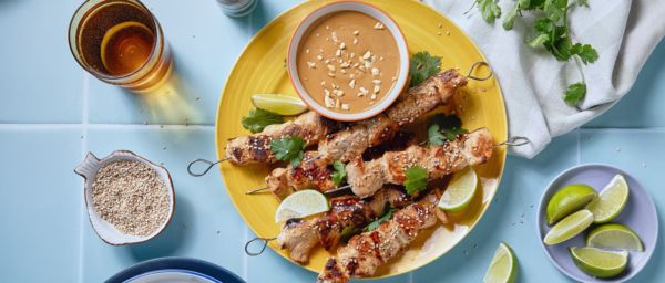 Chicken satay skewers with peanut sauce served on a plate with a dressed table