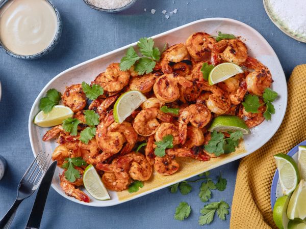 Grilled shrimp with lime wedges on a blue plate which is surrounded by tableware