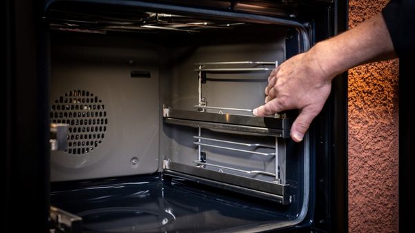 Ръка бърка в празна фурна, от която са извадени решетките и аксесоарите