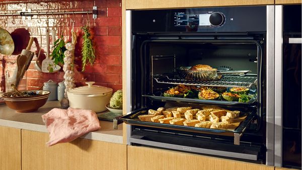 Отворена фурна с издърпани решетки, разкриващи различно ястие на всяко ниво: печено на горната решетка, след това пълнена тиква и предястие на долната.