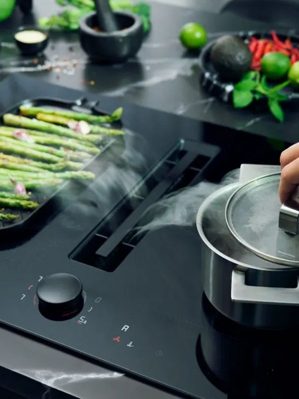 Kookplaat met afzuiging waarop een grillpan groene asperges bakt en een pan water aan de kook wordt gebracht