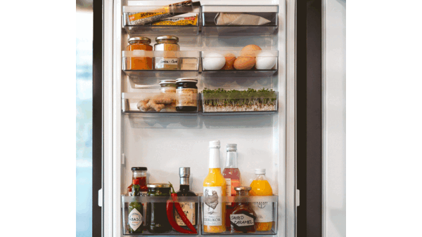 Un frigorifero con barattoli, cartoni di uova, erbe aromatiche, latte e altre bottiglie, tutto perfettamente in ordine e con un aspetto invitante.