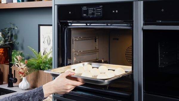 Person placing a tray of uncooked pork buns into a steam oven for cooking.