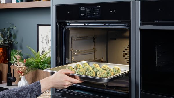 Person placing a tray of uncooked spinach and cheese dumplings into a steam oven for cooking.