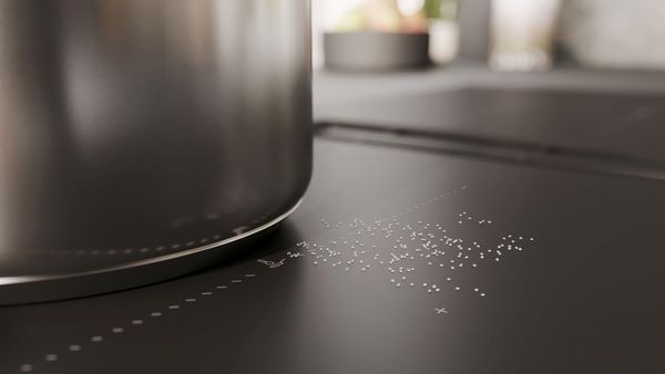 Primo piano di un piano nero ed elegante con una pentola in acciaio, con granelli bianchi sparsi qua e là ed elementi di design in stile minimal.