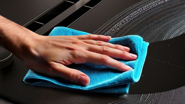 Una mano pulisce un piano con un panno in microfibra blu, lasciando una serie di scie trasparenti sulla superficie lucida.