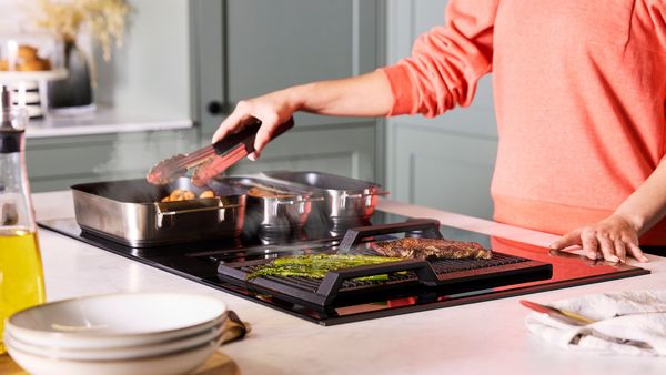 Woman using tongs to turn meat in the Flex Pan