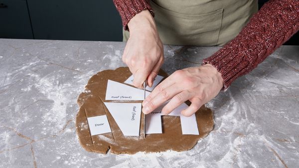 Rolled out gingerbread dough being cut into shapes with stencils.