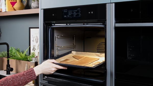 Cut gingerbread pieces on a baking tray being placed into an open oven.