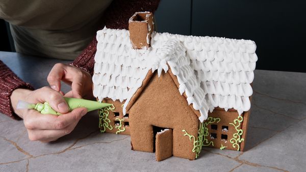 Icing being piped onto a finished gingerbread house for decoration.
