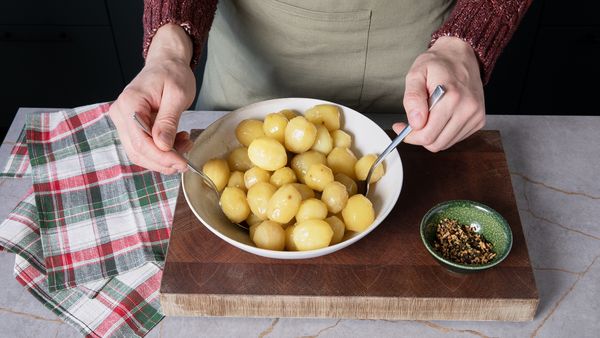Peeled potatoes being tossed in a large bowl with oil, rosemary and garlic.