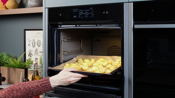 A baking tray of peeled potatoes being placed into an open oven.