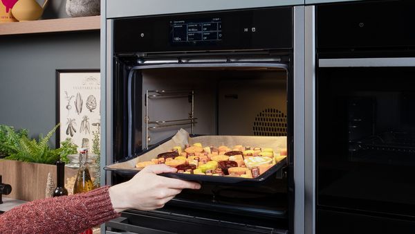 A baking tray of colorful root vegetables being placed into an open oven.
