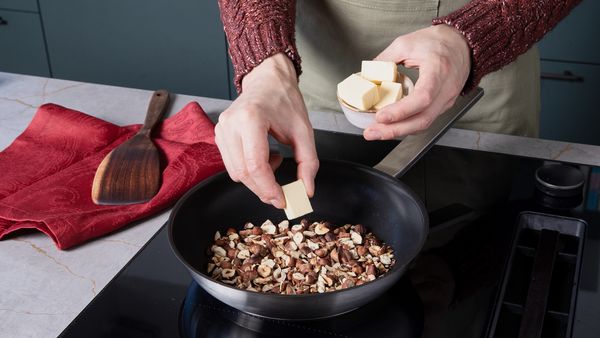 Hazelnuts toasting in a pan on the stovetop as butter is added.