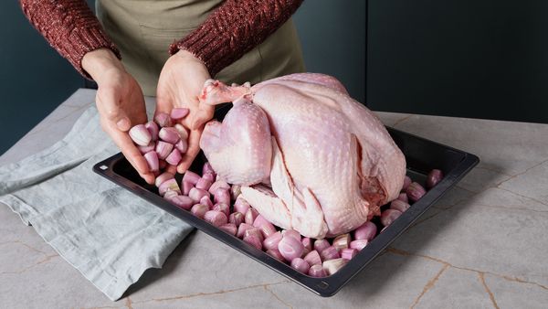 Shallots being placed onto a baking tray with a whole raw turkey.