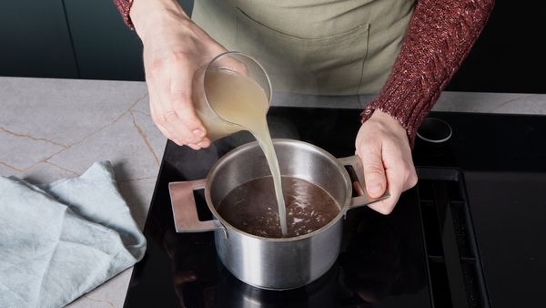 Gravy simmering in a pot on the stovetop, chicken stock being poured in while whisking.
