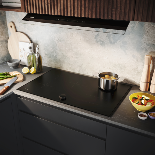 Matzwarte kookplaat met pan aardappelen en andere ingrediënten op een zwart marmeren werkblad.