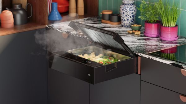 Cassetto per cottura a vapore NEFF aperto e integrato nel piano della cucina, con verdure all&rsquo;interno