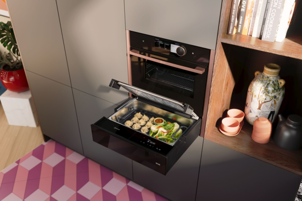 NEFF Dampf-Schublade in moderner Küche – platzsparend unter einem Backofen eingebaut, mit geöffnetem Glasdeckel und aufsteigendem Dampf beim Garen von frischem Gemüse.
