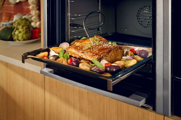 NEFF oven with meat probe inserted in tray of roast meat and vegetables.