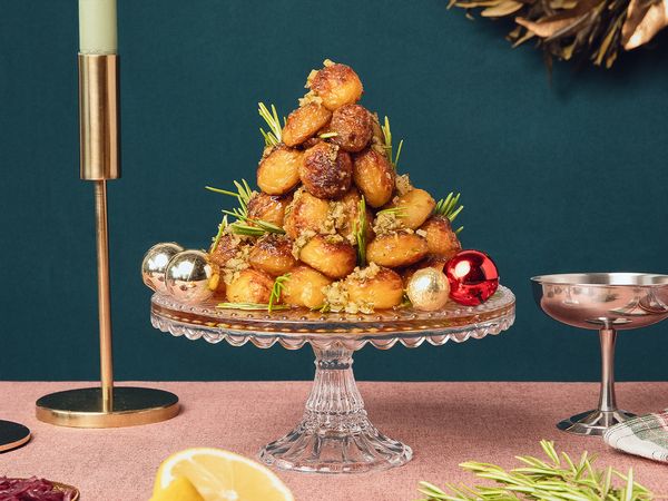 Golden crispy roast potatoes arranged in a cone shape on a cake stand in a modern christmas setting. 