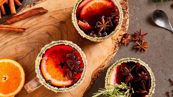 Чаши греяно вино с подправки и портокали върху дървена дъска.