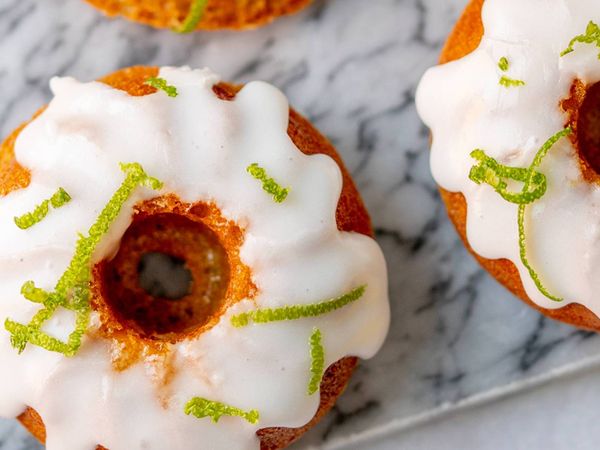 Sliced dessert on dark plates, topped with nuts, orange slices, and powdered sugar, surrounded by hazelnuts and utensils.