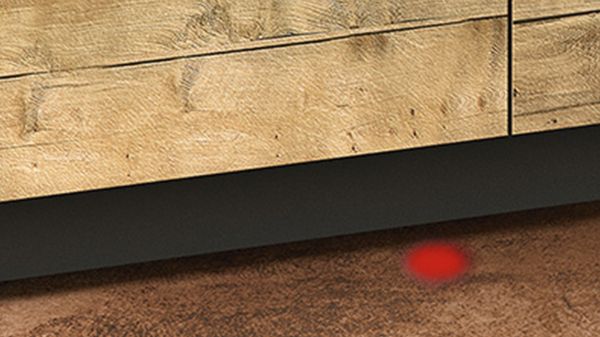 Едър план на дървен шкаф с тъмна основа, с отражение на червена светлина върху пода.