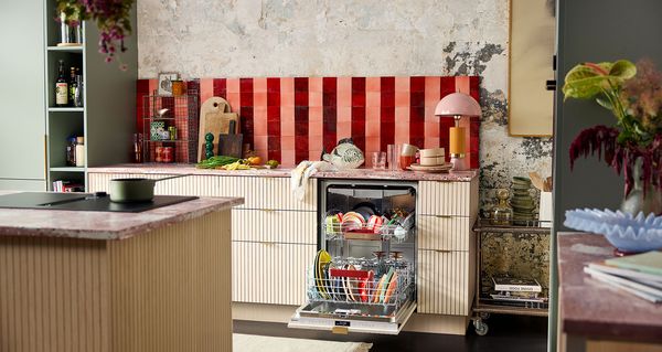 Moodne köök, kus nõudepesumasin on täis värvilisi taldrikuid ning tööpind on täidetud köögiviljade ja köögiriistadega.