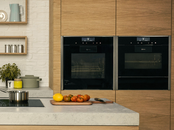 Een moderne keuken met twee strakke zwarte ovens van NEFF en een houten snijplank met verse tomaten en een citroen.