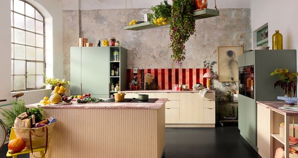 Светла, модерна кухня със зелени шкафове, яркочервен гръб, изобилие от продукти и велосипед, облегнат на стената.