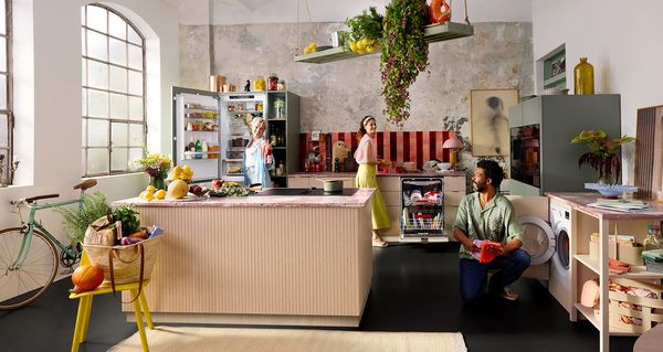 Una cucina moderna con arredamento vivace e vegetazione lussureggiante, dotata di un'isola, frigorifero aperto e un'accogliente zona pranzo.