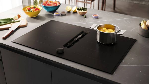 A close-up of a sleek, black countertop with a metallic pot, featuring scattered white granules and minimalist design elements.
